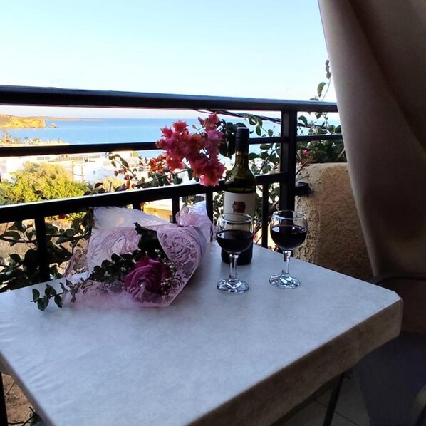 A balcony with a table, a bottle of wine, two wine glasses, and a bouquet of flowers.