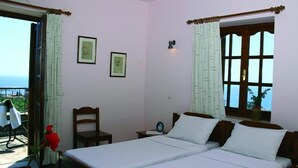A bedroom with two beds, a window with curtains, a chair, a table, and a view of the sea.