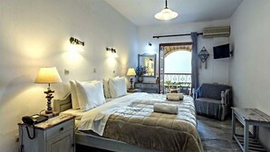 A bedroom with a bed, bedside lamps, a nightstand, a chair, a small table, and a balcony with a view.