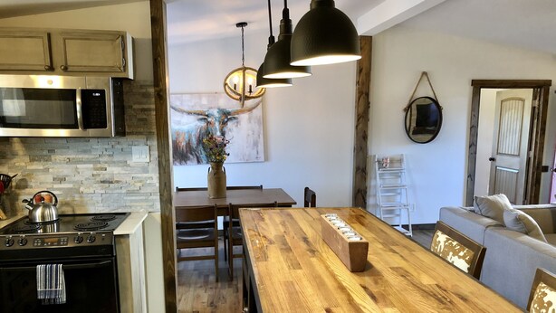 A modern kitchen with a wooden dining table, a built-in oven, and a stone backsplash. - Nolia Cabin in the Little River Valley (Nashoba)