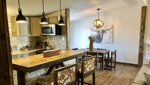 A modern kitchen with a wooden island, pendant lights, and a dining area with wooden chairs. - Nolia Cabin in the Little River Valley (Nashoba)