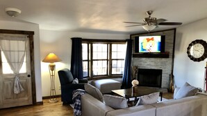 A living room with a sofa, a coffee table, a TV, a fireplace, and a ceiling fan. - Nolia Cabin in the Little River Valley (Nashoba)