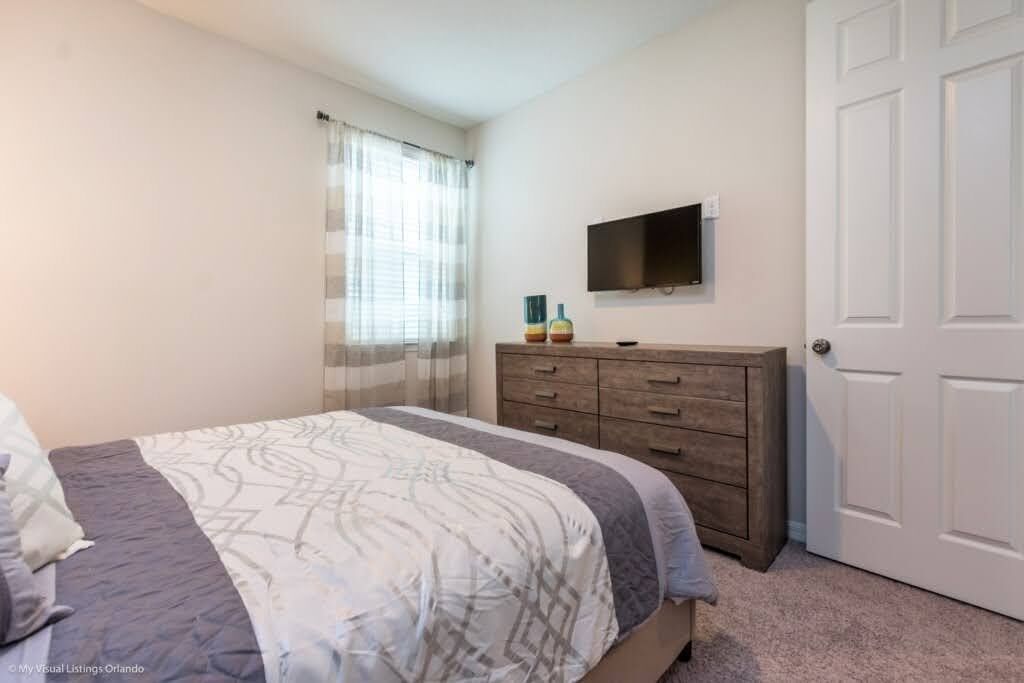 A bedroom with a bed, a dresser, a television on the wall, and a door.
