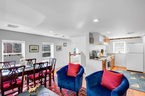 A modern living room with a dining area, a kitchen, and a staircase leading to an upper floor. - Sweet Retreat (Marblehead)