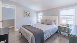 A bedroom with a bed, a dresser, a nightstand, a painting, and a window.