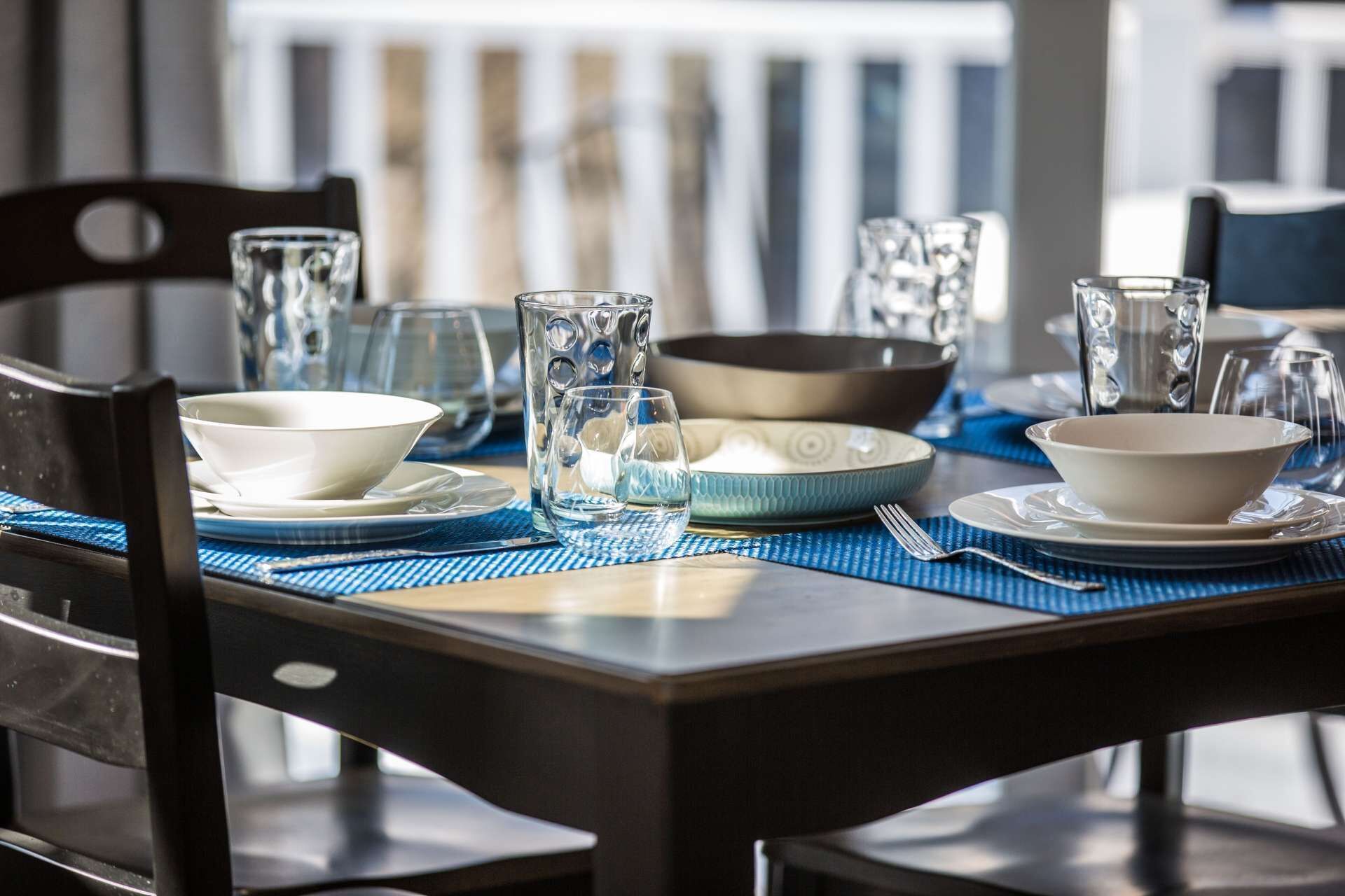 A dining table set with clear glassware, bowls, and plates on a blue placemat.