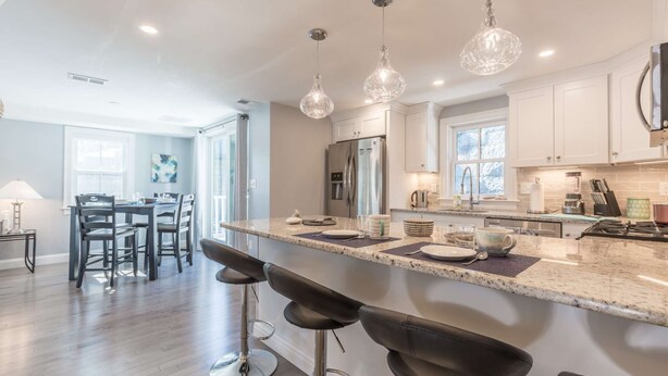 A modern kitchen with a large island, bar stools, stainless steel appliances, and pendant lighting.
