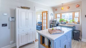 Una cocina moderna con armarios blancos, una isla central y vista a la calle a través de amplios ventanales.