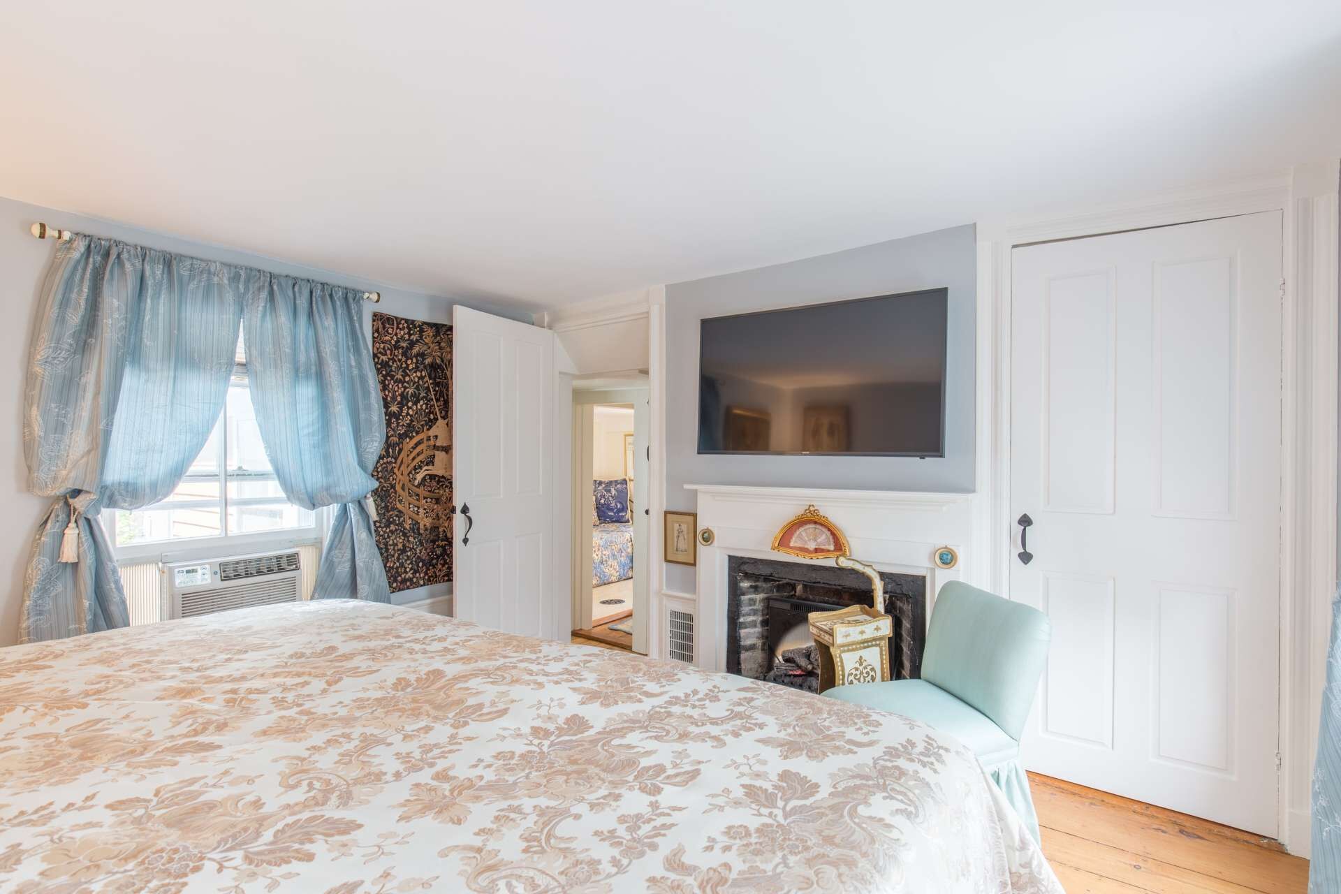 Un dormitorio con una cama grande, una chimenea, un televisor montado en la pared y una puerta.