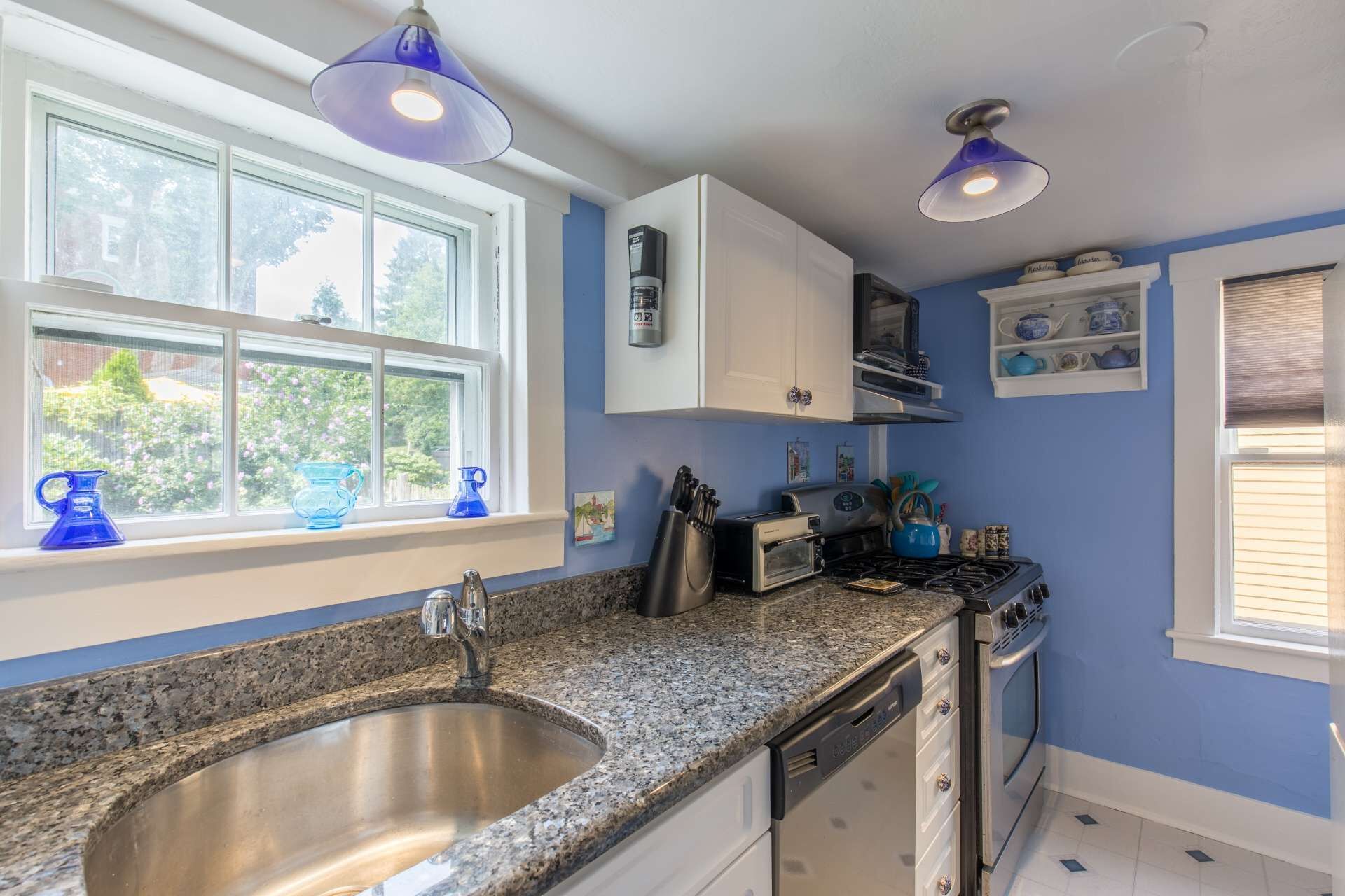 A kitchen with granite countertops, a stainless steel sink, white cabinets, a toaster, a kettle, and a coffee maker.