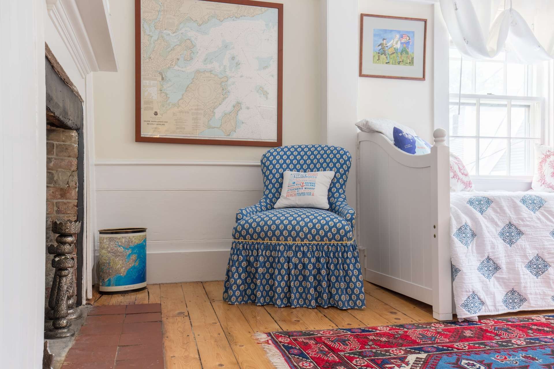 Una habitación con un sillón estampado, un mapa en la pared, un cuadro enmarcado y una cama con cubrecama estampado.