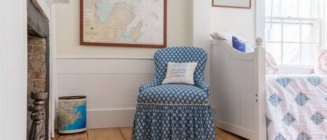 Una habitación con un sillón estampado, un mapa en la pared, un cuadro enmarcado y una cama con cubrecama estampado.