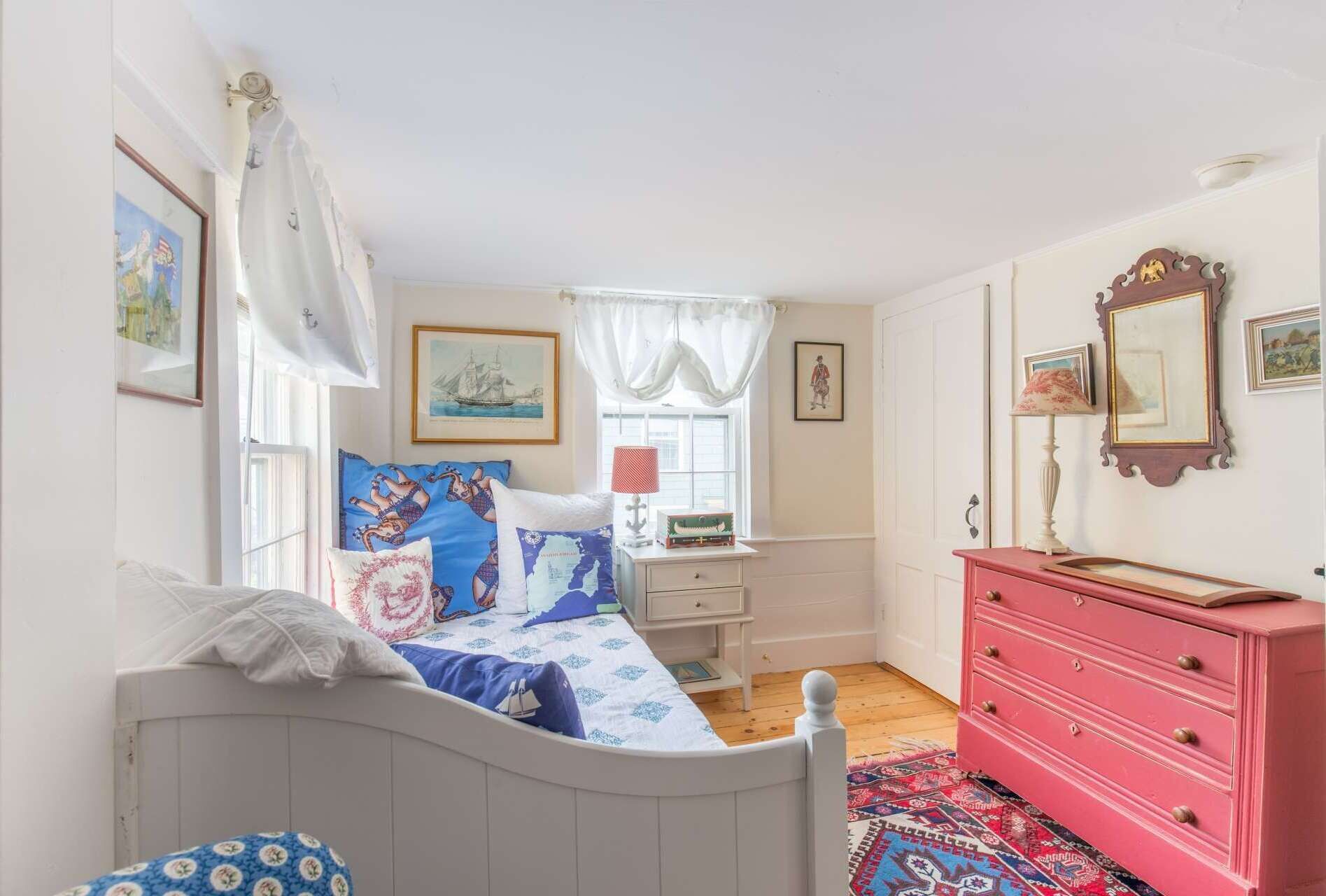A bedroom with a bed, a dresser, a nightstand, and a window with curtains.
