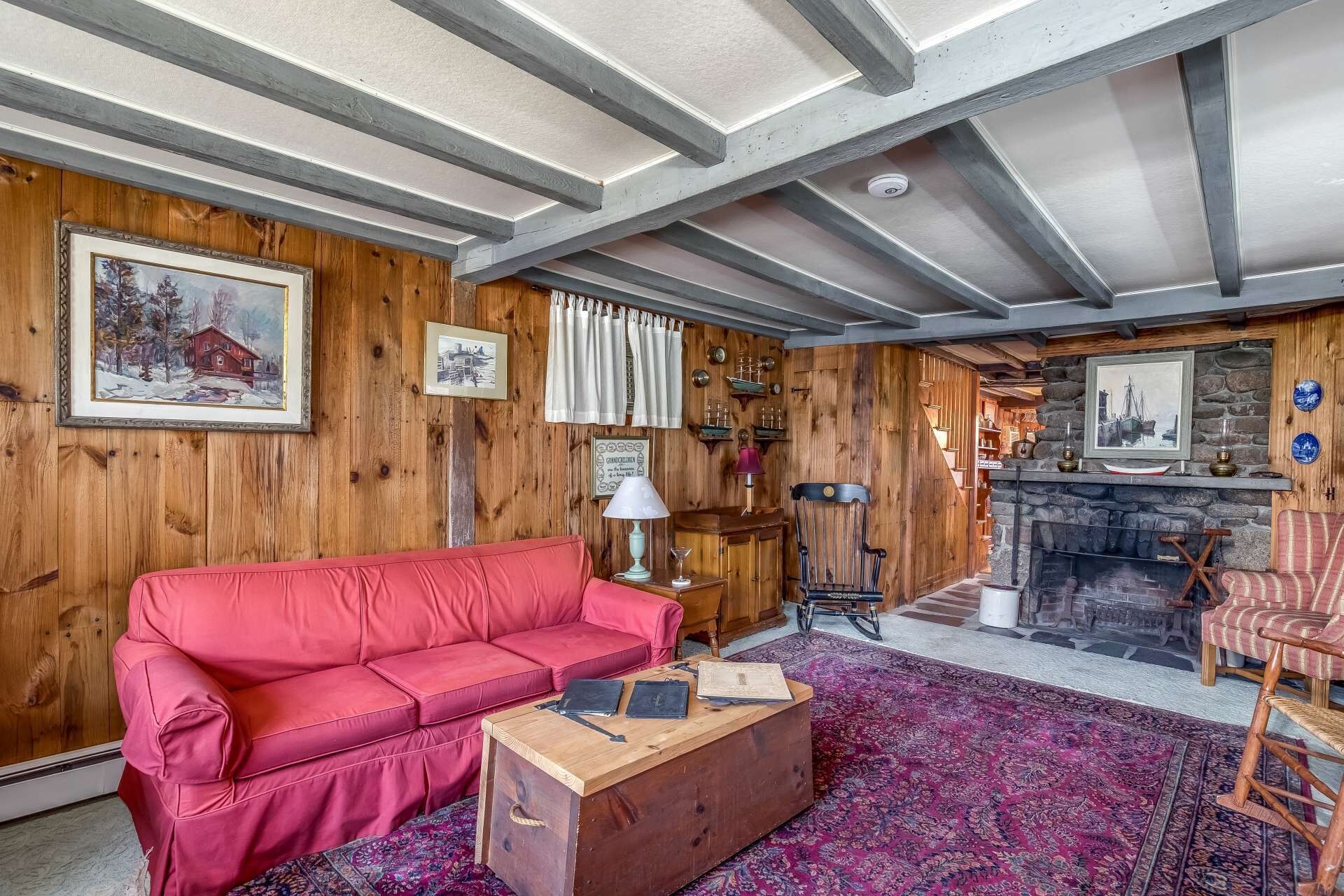 A cozy living room with a red sofa, a wooden coffee table, a fireplace, and wooden walls.