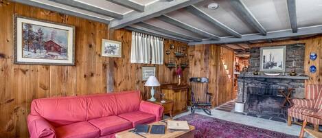 A cozy living room with a red sofa, a wooden coffee table, a fireplace, and wooden walls.