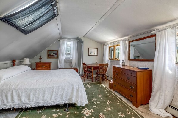 A bedroom with a bed, a dresser, a mirror, a table, and a chair. - Bell Buoy (Rockport)