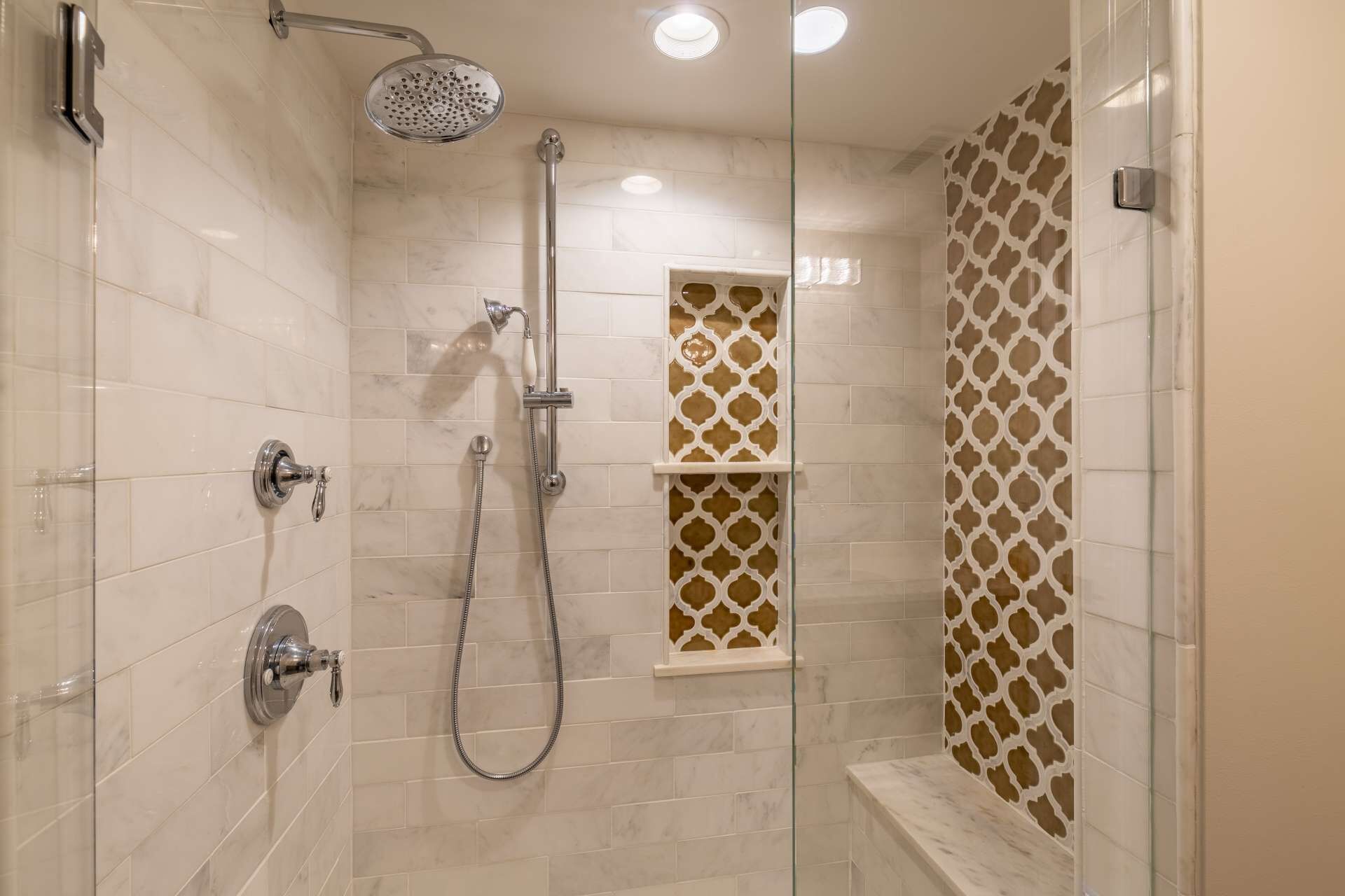 A shower with a handheld showerhead, a wall-mounted faucet, and a glass-enclosed shower stall.
