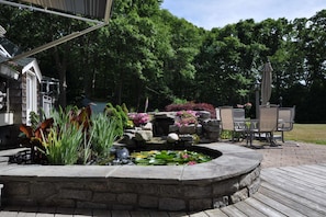 A stone fountain with water lilies and flowers, surrounded by a wooden deck and outdoor furniture.