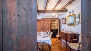 A dining area with a wooden table set for four, flanked by chairs with striped upholstery. A wooden cabinet with glassware is visible in the background. - Rockmere Inn (Marblehead)