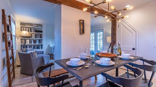 Un coin repas avec une table en bois foncé, dressée pour quatre personnes, entourée de chaises en bois foncé. Un lustre moderne aux ampoules apparentes est suspendu au-dessus.