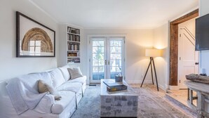 Un salon avec un canapé blanc, une bibliothèque, une table basse, un lampadaire et un téléviseur.