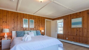 A bedroom with a large bed, wooden paneling, two bedside lamps, a door leading outside, and a framed picture on the wall. - Blue Star (Salisbury)