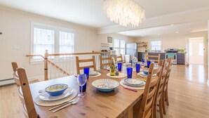 A spacious dining area with a wooden table set for six, surrounded by chairs. A modern chandelier hangs above, and the room has large windows allowing natural light. - Blue Star (Salisbury)