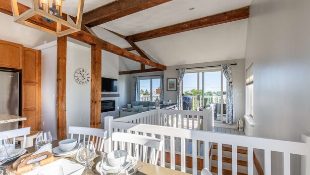 Un coin repas avec une table dressée pour quatre personnes, un téléviseur fixé au mur et un balcon offrant une vue sur l’extérieur.