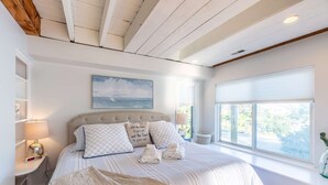 Une chambre à coucher avec un grand lit, une tête de lit, une table de chevet, une lampe, une fenêtre et un tableau au mur.
