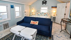 A compact bedroom with a bed, a blue sofa, a small table, and a ceiling fan.