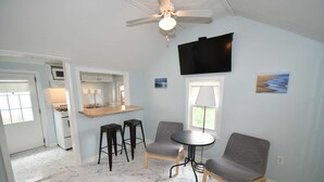 A compact kitchen with a dining area, a ceiling fan, and a TV mounted on the wall.
