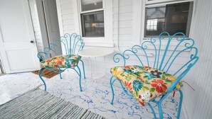 A porch with two blue metal chairs with floral cushions, a small round table, and a white door.