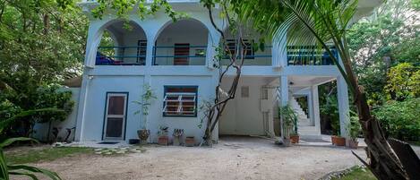 A two-story building with a white exterior and blue accents, surrounded by greenery.