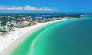 Un paisaje urbano costero con una playa extensa, aguas turquesas cristalinas y un horizonte de edificios.