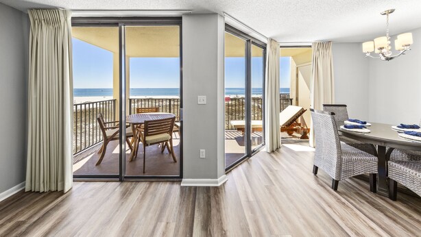 Una camera d'hotel con balcone vista spiaggia, un'area pranzo con sedie in vimini e un lampadario.
