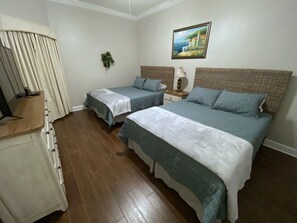 A hotel room with two beds, a wooden dresser, a painting on the wall, and a potted plant.