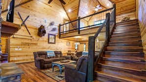 A cozy log cabin interior with a wooden staircase, a plush sofa, and a fireplace. - Whitetail Ridge Has Unbelievable Views Overlooking Beavers Bend State Park (Broken Bow)