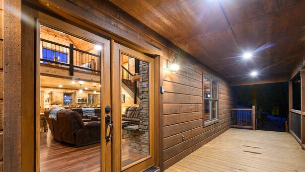 A wooden cabin with a covered deck, a stone fireplace, and a two-story interior with a sofa and dining area. - Whitetail Ridge Has Unbelievable Views Overlooking Beavers Bend State Park (Broken Bow)