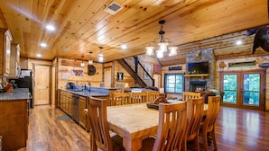A wooden interior with a dining area, kitchen, and fireplace. - Whitetail Ridge Has Unbelievable Views Overlooking Beavers Bend State Park (Broken Bow)