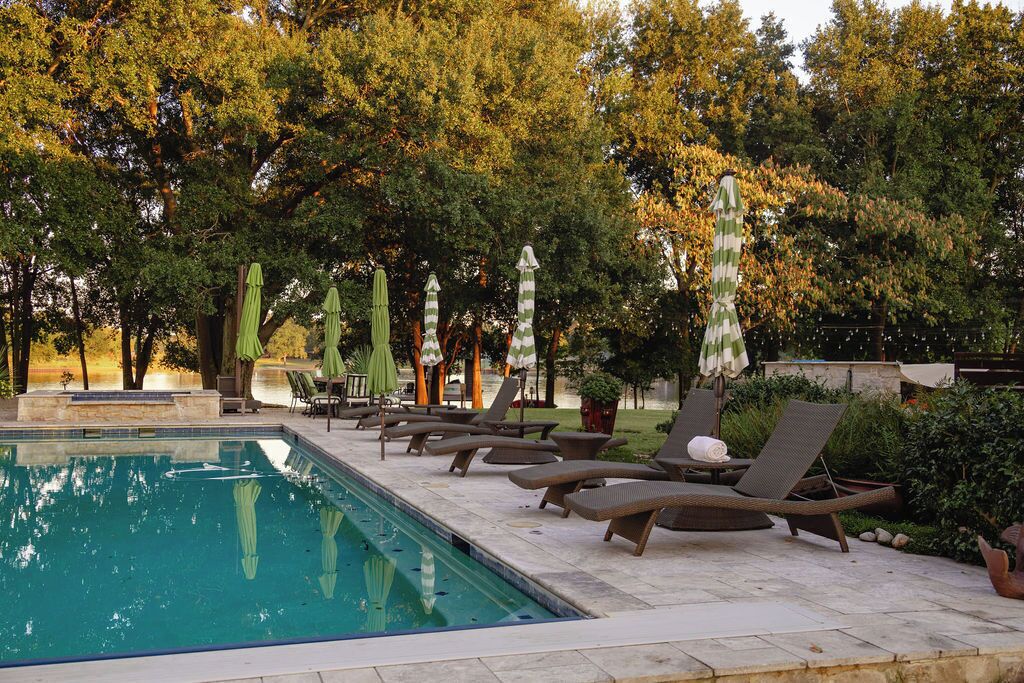 Un área junto a la piscina con sillones de descanso y sombrillas, rodeada de árboles.