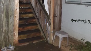 A wooden staircase leading to a second floor, a white wall with a window, and a small white stool.