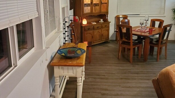 A compact kitchen with a dining area, featuring a wooden cabinet, a small table with chairs, and a window with blinds.