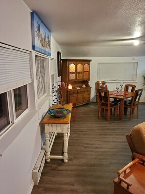 A compact kitchen with a dining area, featuring a wooden cabinet, a small table with chairs, and a window with blinds.