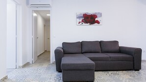 A living room with a gray sectional sofa, a small ottoman, a red abstract painting on the wall, and patterned floor tiles. - Spacious, Central Apartment – Ideal for families (Salou)