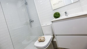 A modern bathroom with a glass shower enclosure, a toilet with a towel on it, and a sink with a green plant. - Spacious, Central Apartment – Ideal for families (Salou)