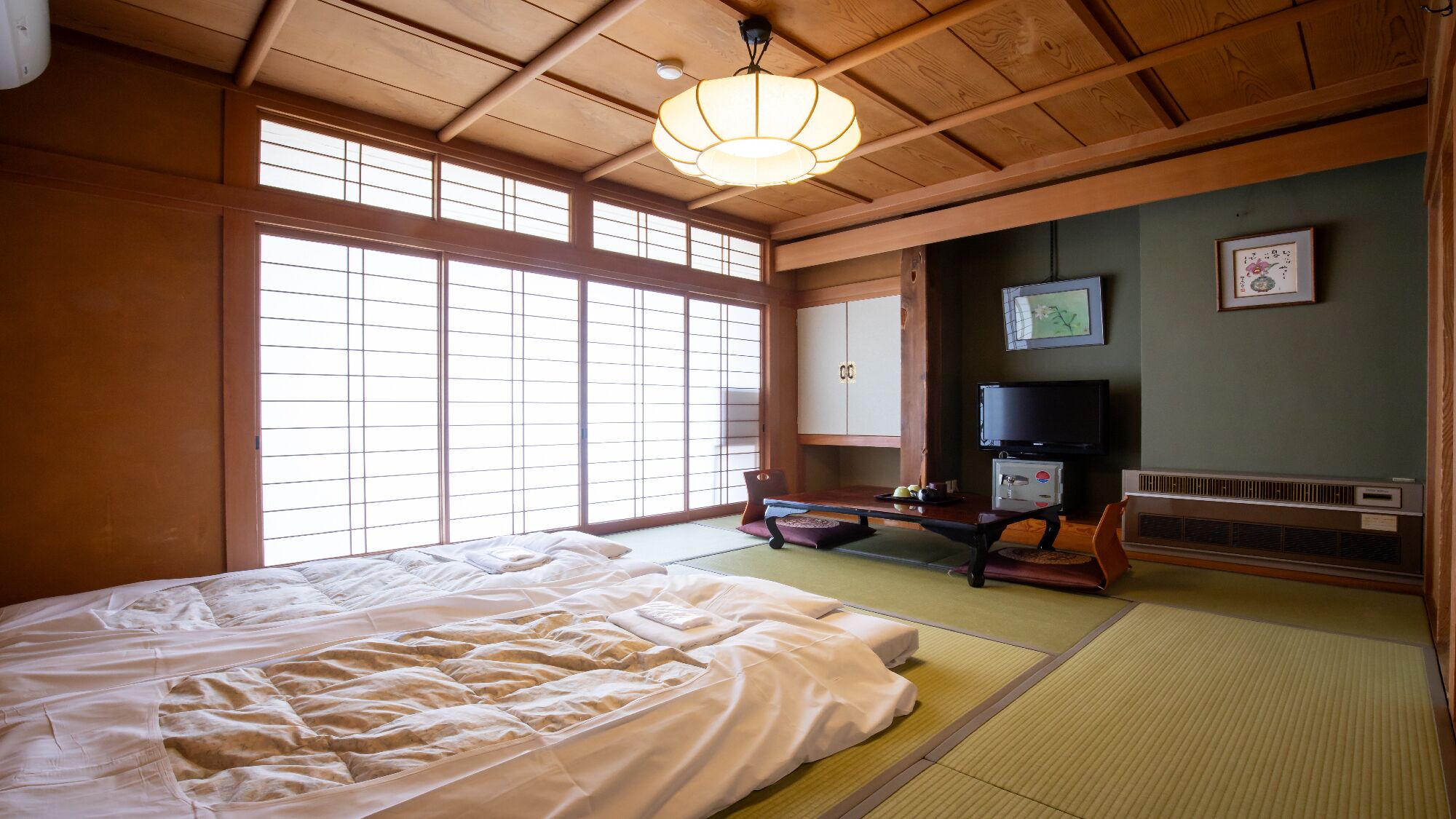 Een traditionele Japanse kamer met tatami vloerbedekking, een bed, een televisie en schuifdeuren.
