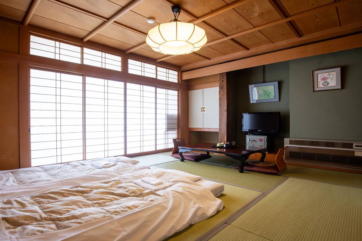 Een traditionele Japanse kamer met tatami vloerbedekking, een bed, een televisie en schuifdeuren.