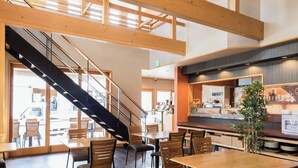 A spacious interior with high ceilings, wooden beams, a staircase, and a dining area with tables and chairs. - Yudanaka Onsen Shimaya (Yamanouchi)