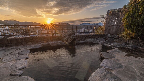 A stone hot spring with a wooden fence and a view of distant mountains at sunset. - Yudanaka Onsen Shimaya (Yamanouchi)