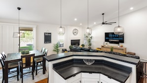 Una cucina moderna con isola a forma di ferro di cavallo, zona pranzo con sedie, televisore e ventilatore a soffitto.